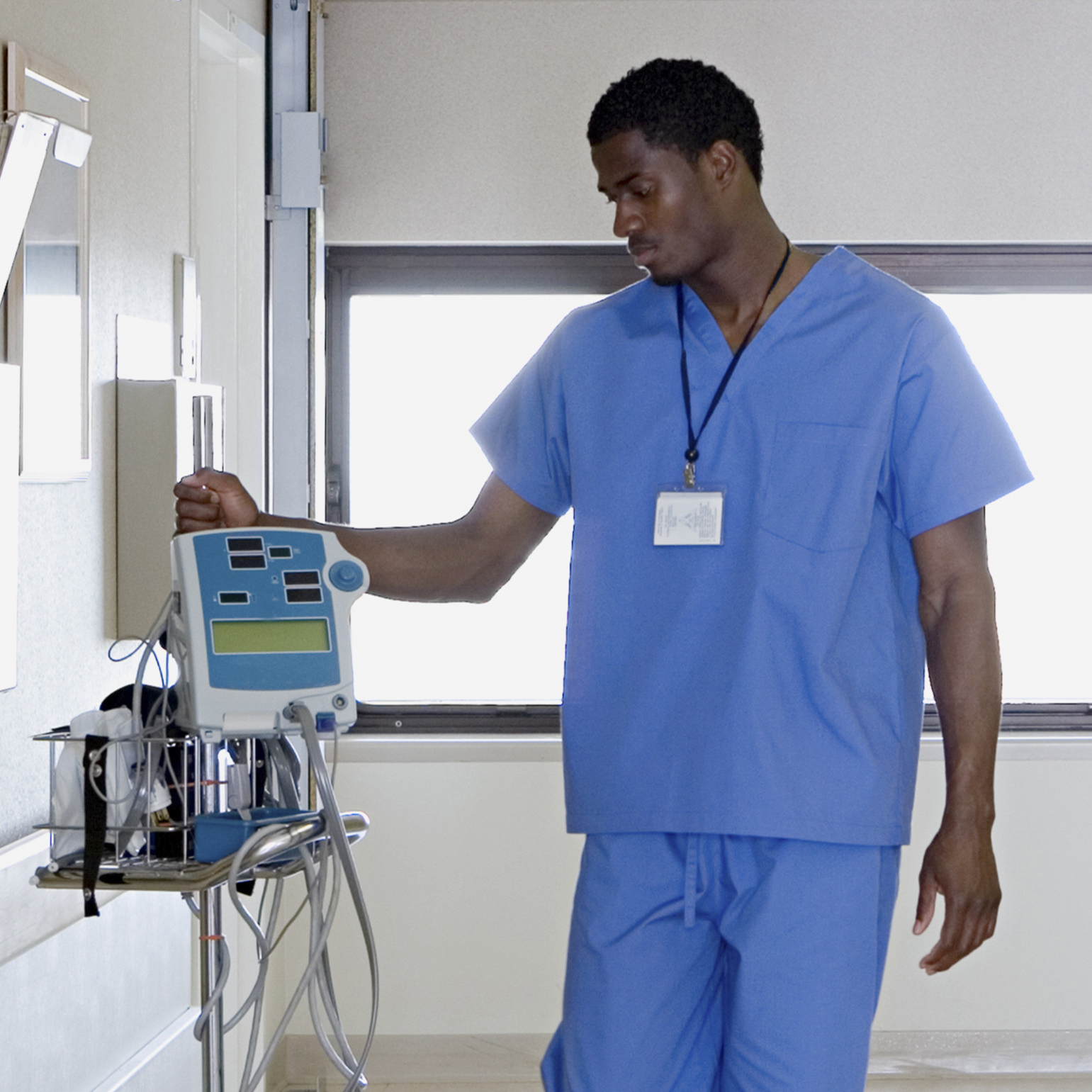 man in scrubs walking in a hospital hallway with IV machine
